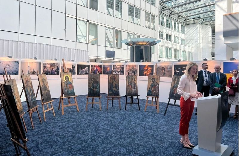 A woman standing in front of several easels with paintings on them.