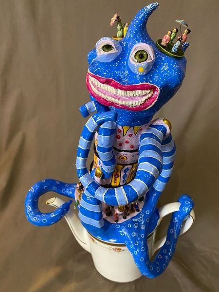 A blue ceramic sculpture of a monkey sitting on top of a cup.