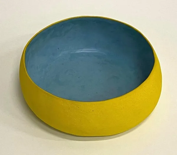 A yellow bowl with blue interior on top of white table.
